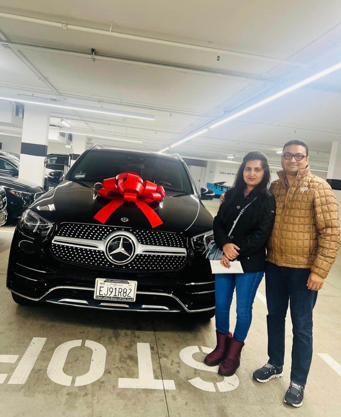 Couple taking delivery of a black Mercedes GLE with a red bow