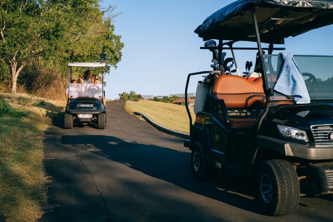 Two golf carts passing on a cart path, one loaded with clubs and a towel