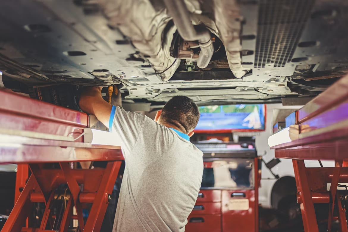 A mechanic working on the underside of a car raised on a workshop lift