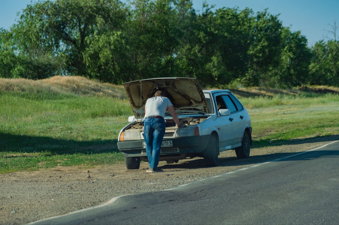 A driver checking under the hood of a car at the roadside