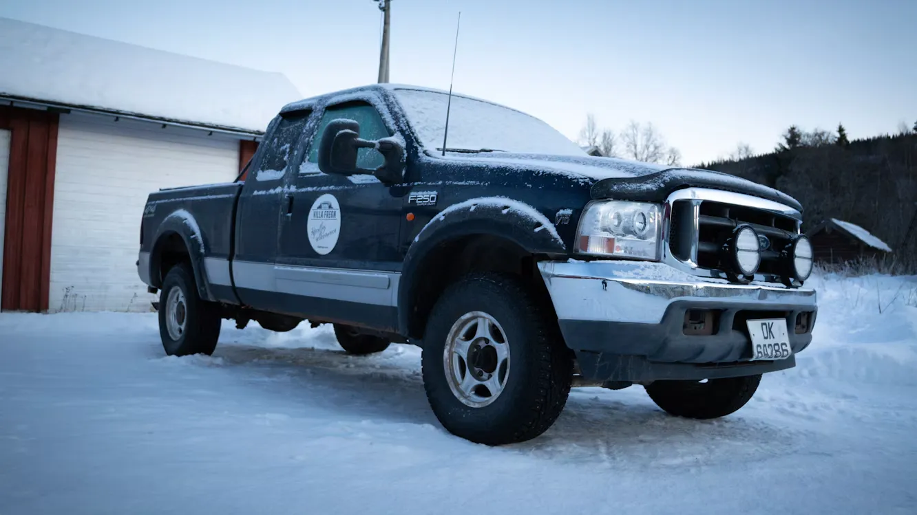 A snow-covered pickup truck parked outside a farm building