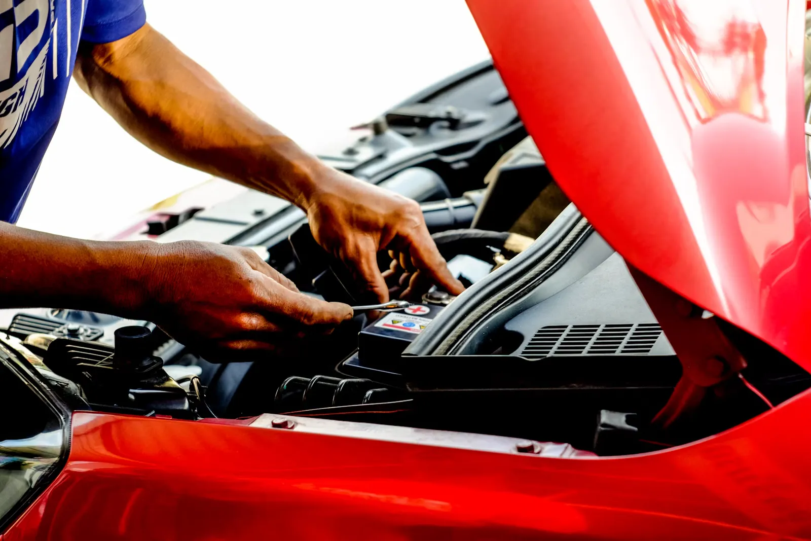 A mechanic working on the engine bay of a red car with the hood raised
